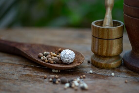 Whole and ground spices with peppercorns, nutmeg, a wooden spoon, and mortar and pestle